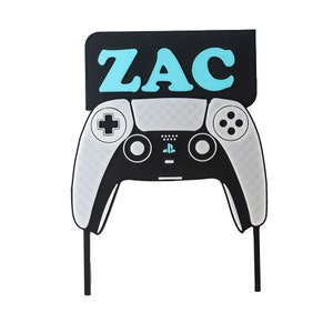 May include: A black and white video game controller with a black sign above it that says "ZAC" in blue letters.