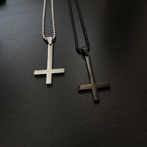 May include: Two silver necklaces with upside down crosses as pendants. One necklace has a silver chain and the other has a black chain.