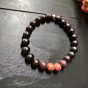 Könnte beinhalten: Ein schwarzes und rotes Perlenarmband mit einem silbernen Akzent. Das Armband besteht aus runden Perlen und hat einen Farbverlauf, der von Schwarz zu Rot übergeht.