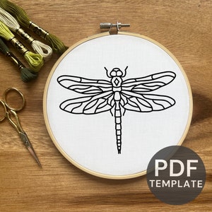 May include: A black and white line drawing of a dragonfly on a white fabric stretched in a wooden embroidery hoop. The hoop is on a wooden surface. The text "PDF TEMPLATE" is below the hoop.