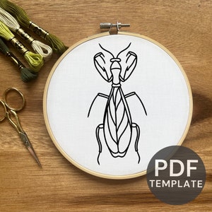May include: A black and white line drawing of a praying mantis on a white fabric background in a wooden embroidery hoop. The text "PDF TEMPLATE" is printed in black on a white background below the hoop.