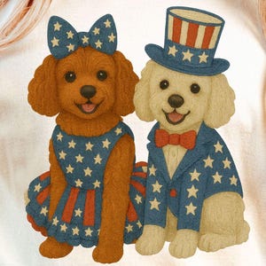 May include: A cream-colored t-shirt featuring two cartoon dogs dressed in patriotic attire. One dog wears a dress and bow with a star pattern, the other a suit and top hat, both in red, white, and blue.