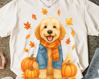May include: White t-shirt featuring a smiling golden retriever wearing a blue denim jacket and orange scarf, surrounded by orange pumpkins and autumn leaves. The shirt has the text "COMFORT COLORS" on the upper right.