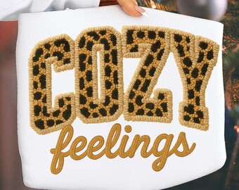 May include: A white rectangular pillow with the words "COZY" and "feelings" embroidered on it. The word "COZY" is in large, block letters with a leopard print pattern. The word "feelings" is in a cursive font.