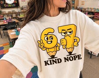 May include: A cream-coloured crewneck sweatshirt featuring a graphic of a yellow number six pencil character making a peace sign and a yellow number seven pencil character giving a thumbs down, with the black text "KIND NOPE" printed below.