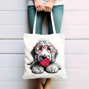 Puede incluir: Bolso tote blanco con una ilustraci&oacute;n en blanco y negro de un perro con gafas rojas en forma de coraz&oacute;n y un coraz&oacute;n rojo. El bolso tiene dos asas blancas. La persona que sostiene el bolso lleva vaqueros azules.
