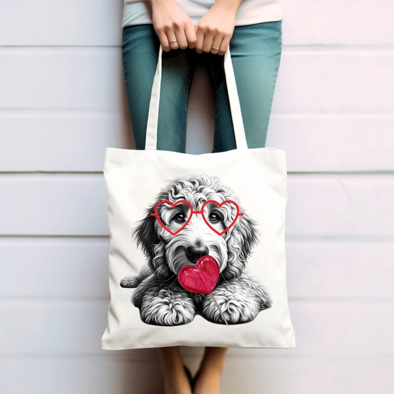 Puede incluir: Bolso tote blanco con una ilustraci&oacute;n en blanco y negro de un perro con gafas rojas en forma de coraz&oacute;n y un coraz&oacute;n rojo. El bolso tiene dos asas blancas. La persona que sostiene el bolso lleva vaqueros azules.