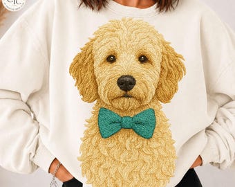 May include: A cream-colored crewneck sweatshirt featuring a large, detailed illustration of a golden-colored curly-haired dog wearing a teal bow tie centered on the front. The dog has dark eyes and a black nose, with textured fur.
