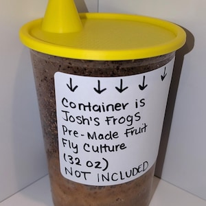 May include: A clear plastic container with a bright yellow lid and a small yellow funnel attachment. A white label on the front features black handwritten text: "Container is Josh's Frogs Pre-Made Fruit Fly Culture (32 oz) NOT INCLUDED" with arrows pointing down.