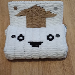May include: White crocheted bag with a brown crocheted top and a smiling face. The bag has black eyes and a black mouth.