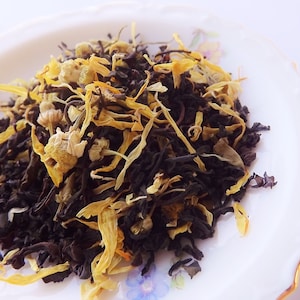 May include: A close-up of a blend of black tea leaves and dried yellow chamomile flowers. The tea is loose leaf and ready to be brewed.