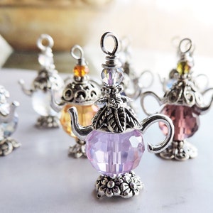 May include: A set of six silver teapot charms with crystal accents. The charms are in various colors, including clear, pink, purple, and yellow.