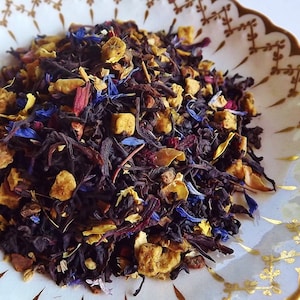 May include: A close-up of a blend of black tea leaves, dried fruit pieces, and flower petals. The tea blend is a mix of black tea, dried apple, dried berries, and cornflower petals.