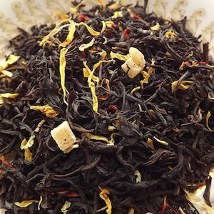 May include: A close-up of a blend of black tea leaves, dried fruit pieces, and flower petals. The tea blend is a mix of black tea, dried mango, and safflower petals.