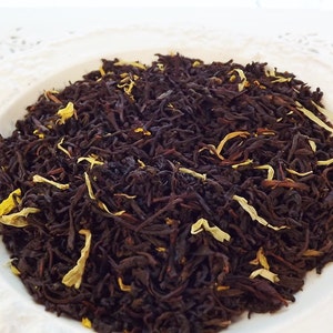 May include: A close-up of a pile of black tea leaves with yellow flower petals. The tea is loose leaf and ready to be brewed.