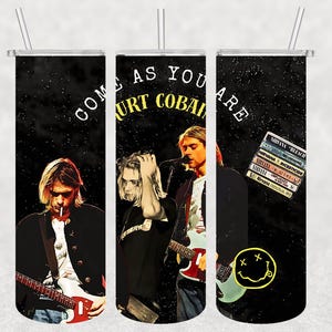 Op de afbeelding: Een zwarte beker met afbeeldingen van Kurt Cobain en de tekst "COME AS YOU ARE KURT COBAIN". De beker bevat ook een smiley en Nirvana albumhoezen. Het heeft een zilveren rietje en deksel.