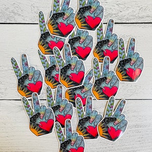 May include: A collection of peace sign stickers. Each sticker features a hand in the peace gesture, with a red heart, floral patterns, and a sunburst design. The background is a light blue with white stars.