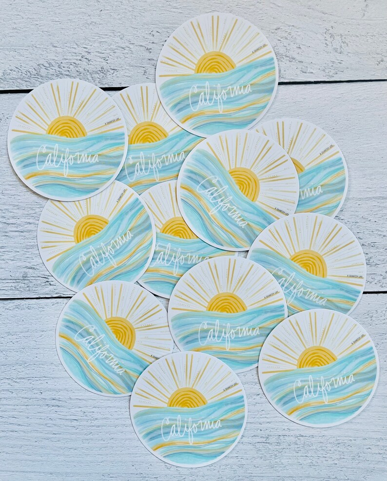 May include: A set of 10 round stickers featuring a stylized sun rising over blue and yellow waves with the word "California" written in white script.