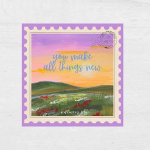 May include: A square art print with a landscape painting inside a lilac postage stamp border. The painting shows a sunset over a field with the words "you make all things new". The artist's name, "a quartzy life", is at the bottom.
