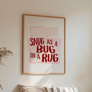 Könnte beinhalten: Schlafzimmer-Interieur mit einem Bett, das mit einer beigen Bettdecke und einer braunen Decke bedeckt ist. Ein gerahmter Druck an der Wand zeigt den Text "Snug as a Bug in a Rug". Dekorative Kissen und ein kleiner hölzerner Beistelltisch mit einer Vase sind ebenfalls zu sehen.