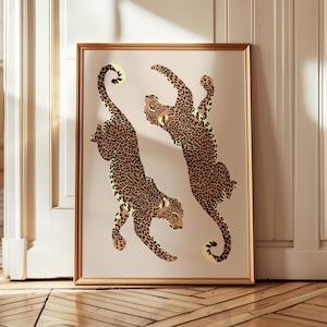 Könnte beinhalten: Gerahmter Kunstdruck mit zwei stilisierten Leoparden mit braunen Flecken auf beigem Hintergrund. Die Leoparden sind in dynamischen Posen dargestellt, vor einem neutralen Hintergrund und in einem goldfarbenen Rahmen. Geeignet für die Inneneinrichtung.