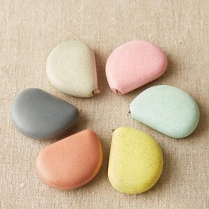 Flat lay of Cocoknits tape measures in clay and linen tones paired with other soft pastel options.