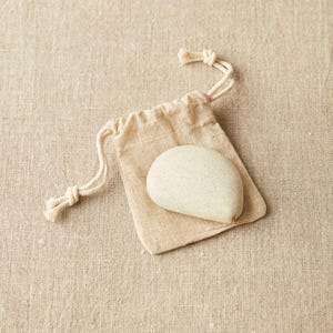 Close-up of Cocoknits tape measure in clay color displayed with its natural linen storage pouch.