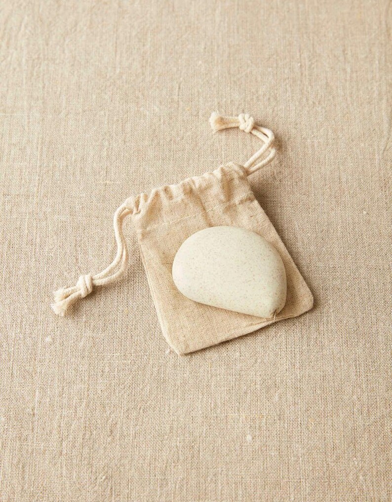 Close-up of Cocoknits tape measure in clay color displayed with its natural linen storage pouch.