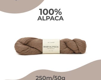 May include: A skein of brown Baby Alpaca yarn, labelled as 100% Alpaca. The label reads "BABYALPACA" and "250m/50g". The yarn is a light brown colour and appears soft. The product is from BC Garn.