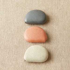 Collection of Cocoknits tape measures in multiple natural colors—clay, linen, yellow, pink, gray, and mint.