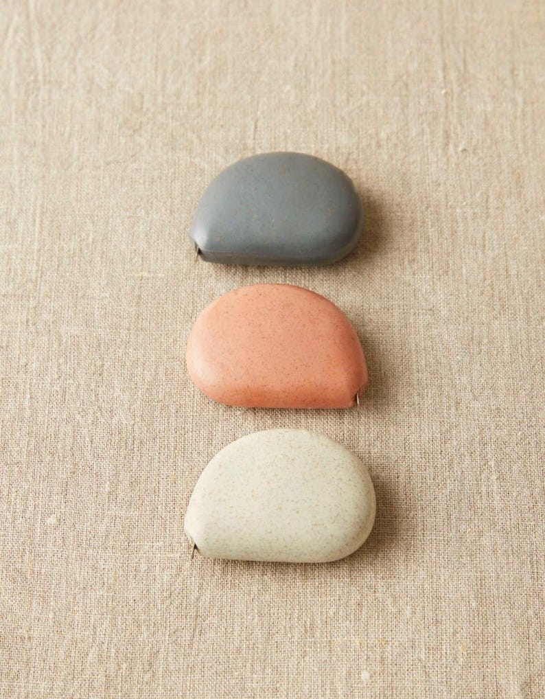 Collection of Cocoknits tape measures in multiple natural colors—clay, linen, yellow, pink, gray, and mint.