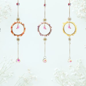 May include: Five hanging crystal suncatchers with a crescent moon charm. Each suncatcher features a different coloured gemstone circle: blue, orange, purple, yellow, and green.