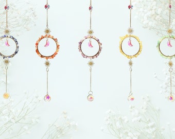 May include: Five hanging crystal suncatchers with a crescent moon charm. Each suncatcher features a different coloured gemstone circle: blue, orange, purple, yellow, and green.