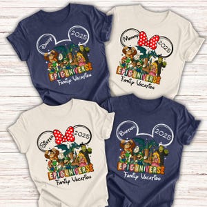 Op de afbeelding: Vier T-shirts met een cartoonafbeelding. Elk shirt heeft de naam van een ander familielid, het jaar 2025 en de tekst "EPICUNIVERSE Family Vacation". De shirts zijn marineblauw en gebroken wit.