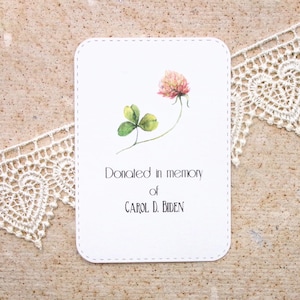 May include: A white card with a pink clover and a green shamrock. The card says "Donated in memory of CAROL D. BIDEN".