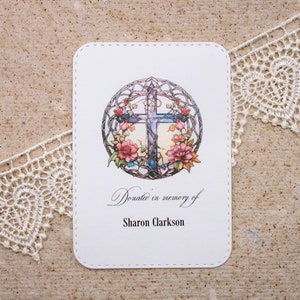 May include: White card with a decorative cross surrounded by flowers and vines. The text reads "Donate in memory of Sharon Clarkson".