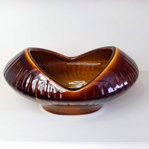 Può includere: Una fioriera in ceramica marrone con apertura a forma di cuore. La fioriera ha una texture a coste sui lati e una finitura lucida. La base è di una tonalità di marrone più scura.