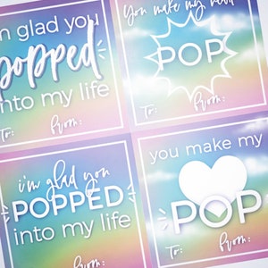 Puede incluir: Cuatro etiquetas de regalo coloridas con un fondo de arcoíris. Las etiquetas tienen el texto "Me alegro de que hayas llegado a mi vida" y "Haces que mi corazón POP".