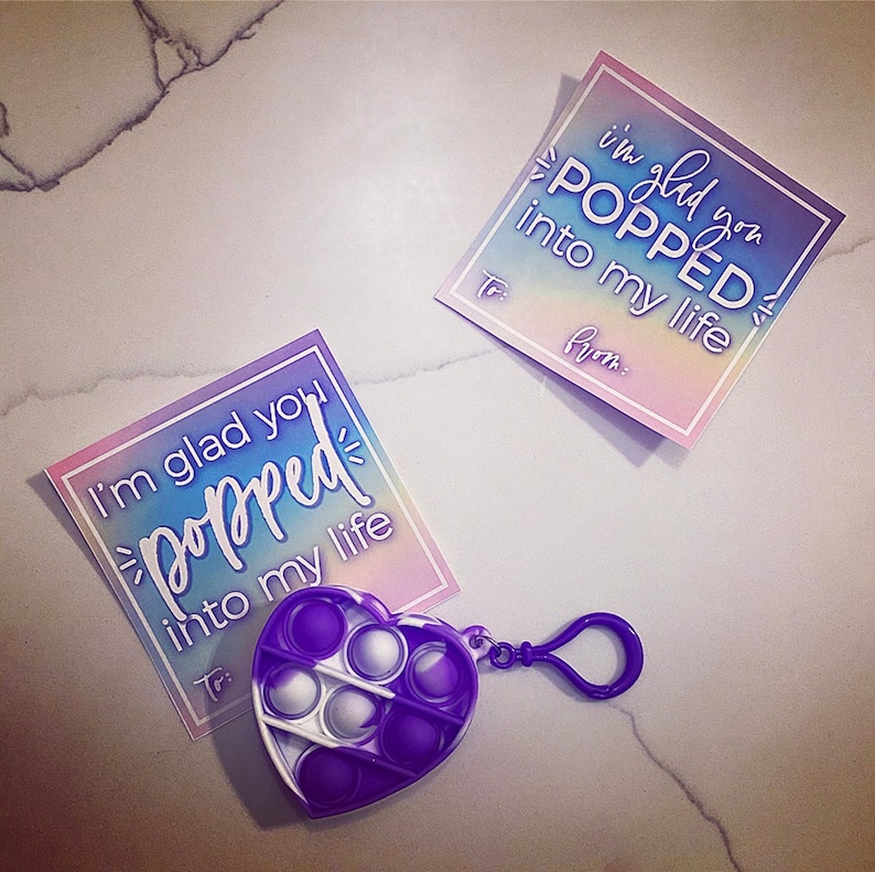 May include: Two rainbow gradient cards with the text "I'm glad you popped into my life" and a purple heart-shaped pop it fidget toy with a silver keychain.