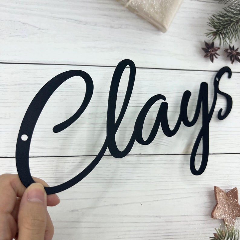 May include: Black metal sign with the word "Clays" written in a cursive font.