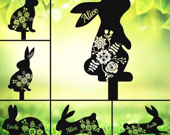 May include: Six black metal silhouette garden stakes featuring bunnies with floral designs. The bunnies are in various poses, including standing, sitting, and hopping. Each stake has a personalized name, including "Alice" and "Emily".