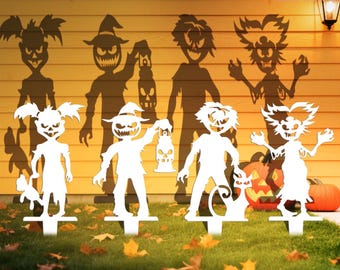 May include: White Halloween yard stakes featuring spooky characters, including a witch, a zombie, and a pumpkin-headed figure. The stakes are placed in a grassy yard with fallen leaves, with shadows of the characters on the wall behind them.