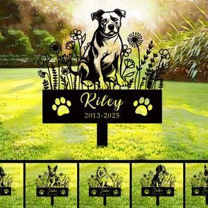 May include: Black metal silhouette of a dog with flowers and the text "Riley 2013-2025" on a black sign. The sign is attached to a metal stake.