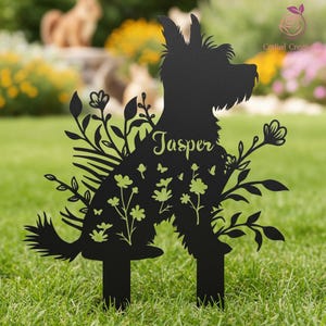 May include: Black metal dog silhouette garden stake with floral and butterfly cutouts. The name "Jasper" is written in green script across the dog's body. The stake is placed in a grassy garden.