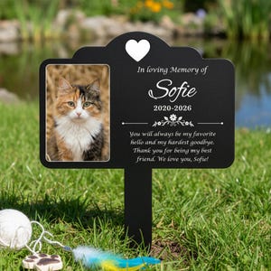 Pode incluir: Uma estaca de jardim comemorativa para animais de estimação em metal preto com uma foto de um gato calico. A estaca tem um coração e o texto "In loving Memory of Sofie 2020-2026." O texto abaixo diz: "You will always be my favorite hello and my hardest goodbye. Thank you for being my best friend. We love you, Sofie!"