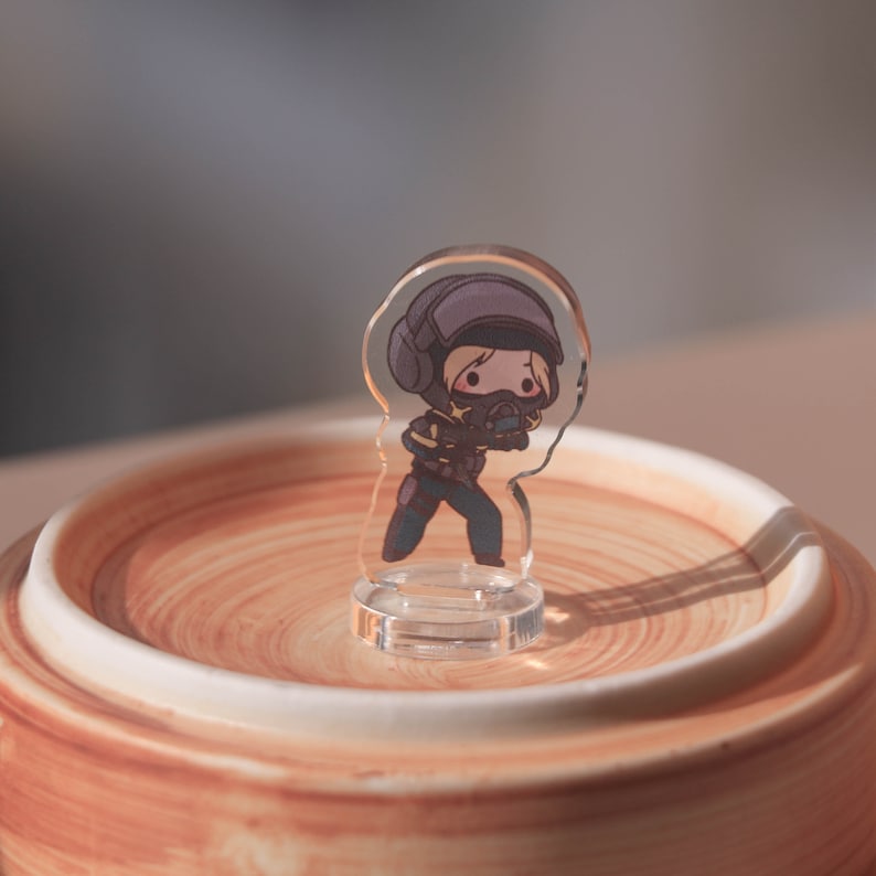 Puede incluir: Una figura de acr&iacute;lico transparente de un personaje de dibujos animados que lleva un casco negro y sostiene un arma. La figura est&aacute; de pie sobre una base de acr&iacute;lico transparente.