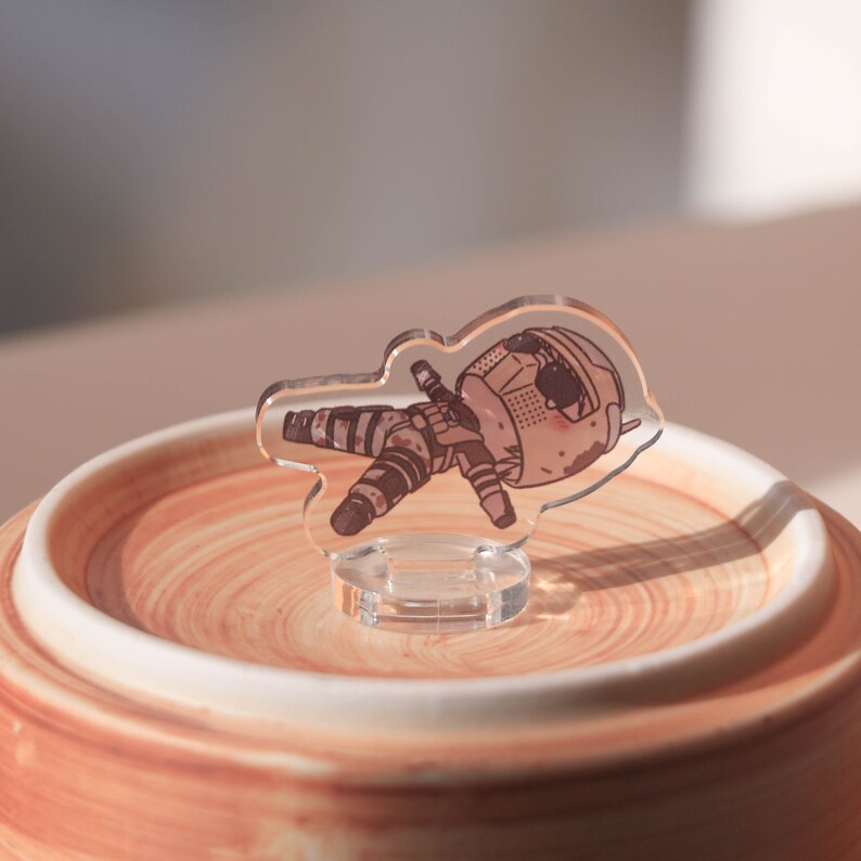 Puede incluir: Una figurita de acr&iacute;lico transparente de un personaje de dibujos animados que lleva un casco y ropa de camuflaje. La figurita est&aacute; sobre una base circular marr&oacute;n.