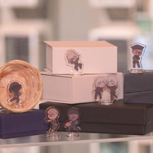 May include: A display of various boxes and decorative items. There are several small, clear acrylic figurines with cartoon character designs. The boxes are in shades of white, navy blue, and black. A woven basket is also present.