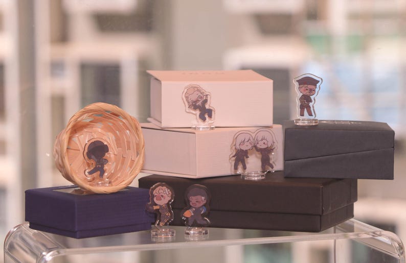 May include: A display of various boxes and decorative items. There are several small, clear acrylic figurines with cartoon character designs. The boxes are in shades of white, navy blue, and black. A woven basket is also present.