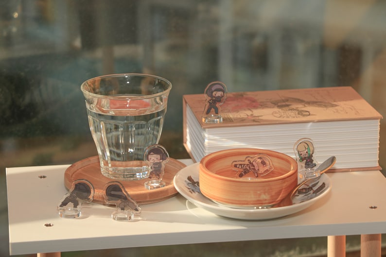 Puede incluir: Una mesa blanca con un vaso de agua, un peque&ntilde;o cuenco de madera, una pila de libros y varias figuritas peque&ntilde;as. Las figuritas son todas personajes diferentes de una caricatura o anime. La mesa est&aacute; puesta sobre una superficie blanca.